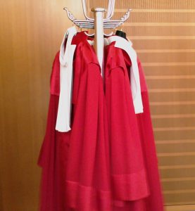 Das Bild zeigt einen Kleiderständer an dem zwei rote Richterroben hängen.